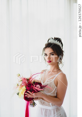 Seductive slender young bride in a sexy lingerie posing on a bed with her bridal bouquet Seductive slender young bride in a sexy lingerie posing on a bed with her bridal bouquet 126370027