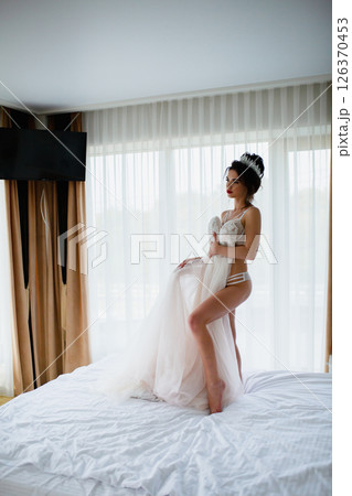 Seductive slender bride in a sexy lingerie posing in a hotel room with her bridal dress 126370453