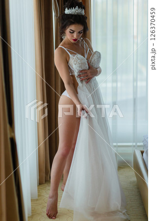 Seductive slender bride in a sexy lingerie posing in a hotel room with her bridal dress Seductive slender bride in a sexy lingerie posing in a hotel room with her bridal dress 126370459