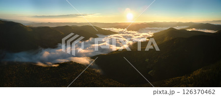Aerial view of bright foggy morning over dark mountain forest trees at autumn sunrise. Beautiful scenery of wild woodland at dawn 126370462