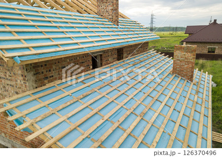 Aerial view of a brick house with wooden roof frame under construction. 126370496