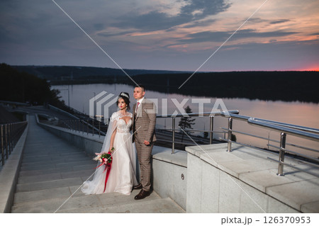 Young beautiful couple of newlywed posing in the evening against the background of an atmospheric panorama and stunning sunset Young beautiful couple of newlywed posing in the evening against the background of an atmospheric panorama and stunning sunset 126370953