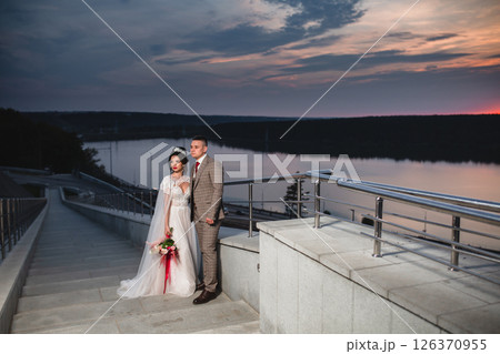 Young beautiful couple of newlywed posing in the evening against the background of an atmospheric panorama and stunning sunset 126370955