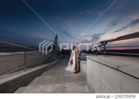 Young beautiful couple of newlywed posing in the evening against the background of an atmospheric panorama and stunning sunset Young beautiful couple of newlywed posing in the evening against the background of an atmospheric panorama and stunning sunset 126370956