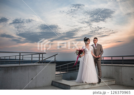 Young beautiful couple of newlywed posing in the evening against the background of an atmospheric panorama and stunning sunset Young beautiful couple of newlywed posing in the evening against the background of an atmospheric panorama and stunning sunset 126370965