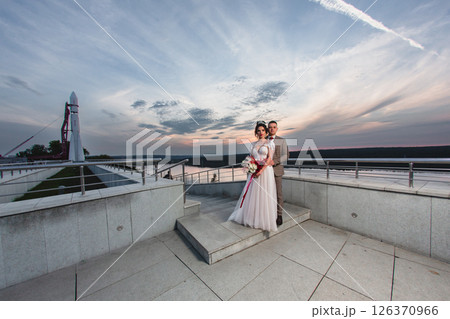 Young beautiful couple of newlywed posing in the evening against the background of an atmospheric panorama and stunning sunset Young beautiful couple of newlywed posing in the evening against the background of an atmospheric panorama and stunning sunset 126370966