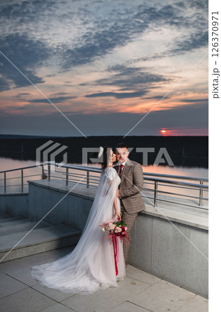 Young beautiful couple of newlywed posing in the evening against the background of an atmospheric panorama and stunning sunset Young beautiful couple of newlywed posing in the evening against the background of an atmospheric panorama and stunning sunset 126370971