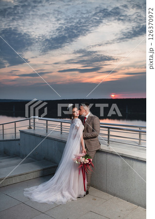 Young beautiful couple of newlywed posing in the evening against the background of an atmospheric panorama and stunning sunset Young beautiful couple of newlywed posing in the evening against the background of an atmospheric panorama and stunning sunset 126370972