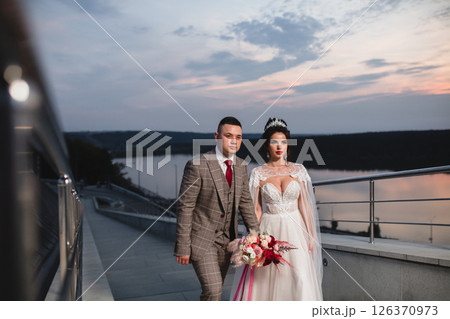 Young beautiful couple of newlywed posing in the evening against the background of an atmospheric panorama and stunning sunset Young beautiful couple of newlywed posing in the evening against the background of an atmospheric panorama and stunning sunset 126370973