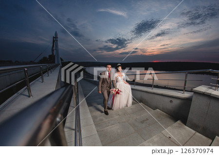 Young beautiful couple of newlywed posing in the evening against the background of an atmospheric panorama and stunning sunset 126370974