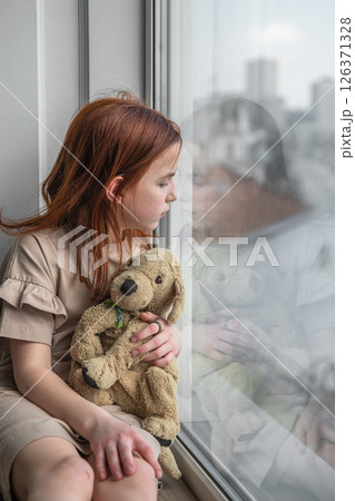 a pensive cute girl sits and looks out the window a pensive cute girl sits and looks out the window 126371328