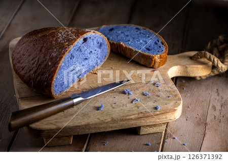 Freshly baked purple bread made with Thai blue ancha tea, partially sliced and resting on a rustic wooden cutting board, looks attractive next to a knife, ready to serve and eat. 126371392