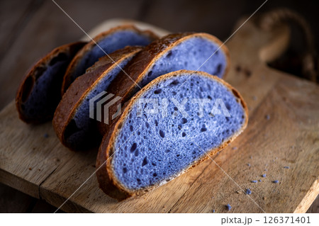 Slices of freshly baked purple bread cooked in blue Thai ancha tea sit on a rustic wooden cutting board, highlighting their vibrant color and unique texture, perfect for food photography. Slices of freshly baked purple bread cooked in blue Thai ancha tea sit on a rustic wooden cutting board, highlighting their vibrant color and unique texture, perfect for food photography. 126371401
