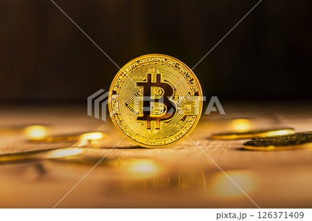 A single gold Bitcoin stands on edge on a wooden surface surrounded by scattered coins, creating a dramatic and luxurious visual representation of cryptocurrency and investment. A single gold Bitcoin stands on edge on a wooden surface surrounded by scattered coins, creating a dramatic and luxurious visual representation of cryptocurrency and investment. 126371409