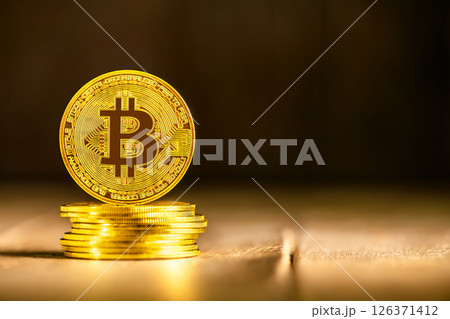 Large, golden physical bitcoin stands on a stack of bitcoins, representing investment, cryptocurrency, and the future of finance against a blurred golden background 126371412