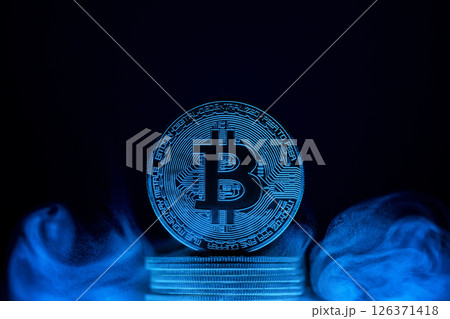 Glowing bitcoin is standing on a stack of coins surrounded by blue smoke on a dark background with copy space, representing the mysterious nature of cryptocurrency 126371418
