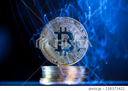 Glowing blue energy is flowing through and around a large, physical bitcoin cryptocurrency coin resting on a stack of coins, representing the dynamic and volatile nature of digital currencies 126371422