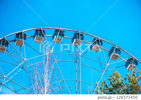 Ferris wheel with empty cabins offers breathtaking views over the amusement park, promising an exciting ride under the vast expanse of a vibrant blue sky 126371450