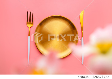 Golden plate with cutlery and spring flowers creating a beautiful table setting on a pink background, perfect for celebrating special occasions or enjoying a springtime meal Golden plate with cutlery and spring flowers creating a beautiful table setting on a pink background, perfect for celebrating special occasions or enjoying a springtime meal 126371722