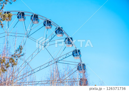 Ferris wheel with empty cabins offers breathtaking views over the amusement park, promising an exciting ride under the vast expanse of a vibrant blue sky 126371736