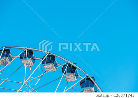 Ferris wheel with empty cabins offers breathtaking views over the amusement park, promising an exciting ride under the vast expanse of a vibrant blue sky 126371743
