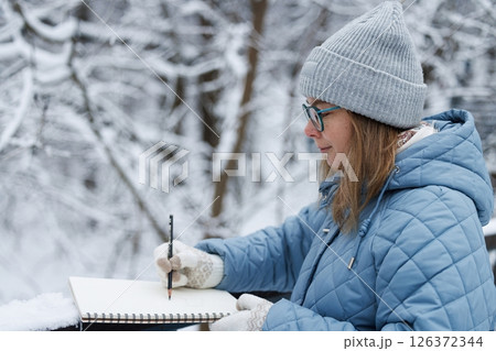 Winter artist capturing serene beauty in snowy forest with sketchbook during a peaceful afternoon 126372344