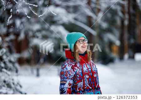 Joyful woman enjoying a snowy winter day while wearing a colorful jacket in a serene forest setting 126372353