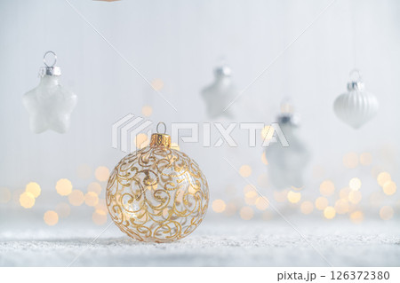 Golden christmas ball ornament resting on a snow-dusted surface, surrounded by hanging star and teardrop ornaments, creating a festive scene with warm bokeh lights Golden christmas ball ornament resting on a snow-dusted surface, surrounded by hanging star and teardrop ornaments, creating a festive scene with warm bokeh lights 126372380