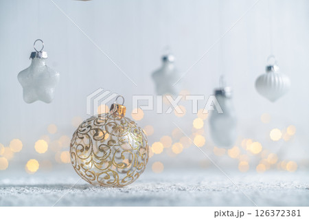 Golden christmas ball ornament resting on a snow-dusted surface, surrounded by hanging star and teardrop ornaments, creating a festive scene with warm bokeh lights Golden christmas ball ornament resting on a snow-dusted surface, surrounded by hanging star and teardrop ornaments, creating a festive scene with warm bokeh lights 126372381