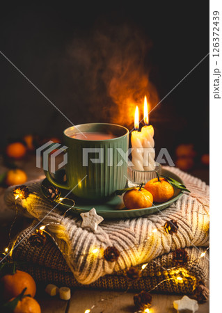 Warm cocoa, burning candles, and tangerines create a cozy atmosphere on christmas or new year's eve, surrounded by glowing lights and pine cones, greeting card Warm cocoa, burning candles, and tangerines create a cozy atmosphere on christmas or new year's eve, surrounded by glowing lights and pine cones, greeting card 126372439