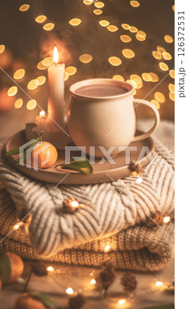Christmas hot chocolate with tangerines and burning candles on a stack of knitted sweaters creates a cozy winter atmosphere with warm bokeh lights, Mocha Mousse 126372531
