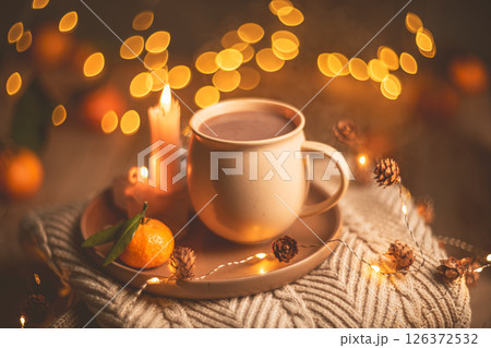Christmas hot chocolate with tangerines and burning candles on a stack of knitted sweaters creates a cozy winter atmosphere with warm bokeh lights Christmas hot chocolate with tangerines and burning candles on a stack of knitted sweaters creates a cozy winter atmosphere with warm bokeh lights 126372532