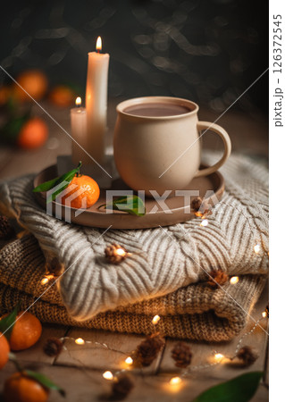 Christmas hot chocolate with tangerines and burning candles on a stack of knitted sweaters creates a cozy winter atmosphere with warm bokeh lights, Mocha Mousse Christmas hot chocolate with tangerines and burning candles on a stack of knitted sweaters creates a cozy winter atmosphere with warm bokeh lights, Mocha Mousse 126372545