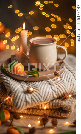 Christmas hot chocolate with tangerines and burning candles on a stack of knitted sweaters creates a cozy winter atmosphere with warm bokeh lights 126372547