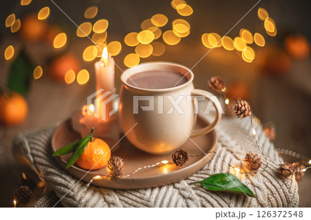 Christmas hot chocolate with tangerines and burning candles on a stack of knitted sweaters creates a cozy winter atmosphere with warm bokeh lights Christmas hot chocolate with tangerines and burning candles on a stack of knitted sweaters creates a cozy winter atmosphere with warm bokeh lights 126372548