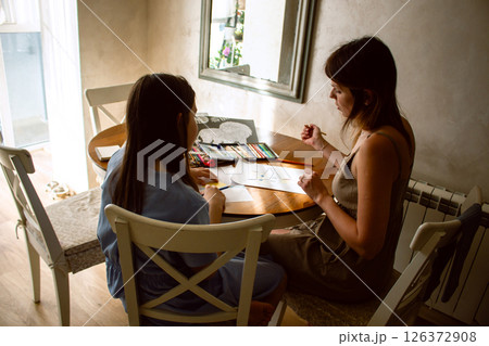 Preteen girl and mom painting together at table shot from behind. Heartwarming moment of family connection. Represents nurturing, childhood development, and family joy in daily life. Preteen girl and mom painting together at table shot from behind. Heartwarming moment of family connection. Represents nurturing, childhood development, and family joy in daily life. 126372908