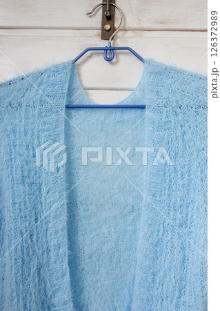 Blue knitted cardigan on hanger on white background. Soft blue knitted sweater in details. Knitting pattern background. Summer knitted fashion. Cozy hobby. Craft product concept. Blue knitted cardigan on hanger on white background. Soft blue knitted sweater in details. Knitting pattern background. Summer knitted fashion. Cozy hobby. Craft product concept. 126372989