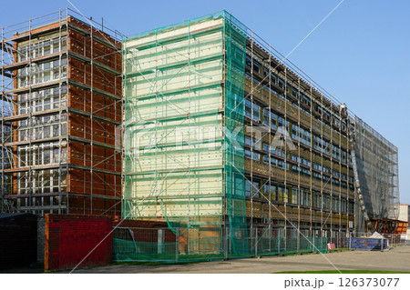 Renovation of office building covered in scaffolding and protective net during reconstruction work Renovation of office building covered in scaffolding and protective net during reconstruction work 126373077