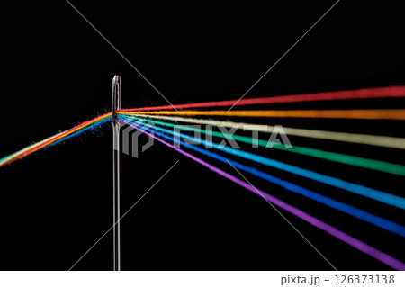 multi-colored threads for sewing in the form of a rainbow pass through an antique needle on a black background 126373138