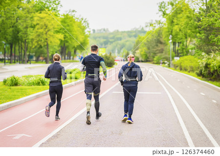 Three active runners move along shared running path in vibrant spring park. Fitness, sport, friendship, group activity, team training, lifestyle concept 126374460