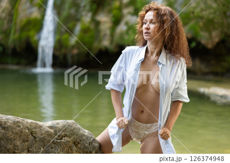 Woman in lace panties and unbuttoned shirt posing by waterfall Woman in lace panties and unbuttoned shirt posing by waterfall 126374948