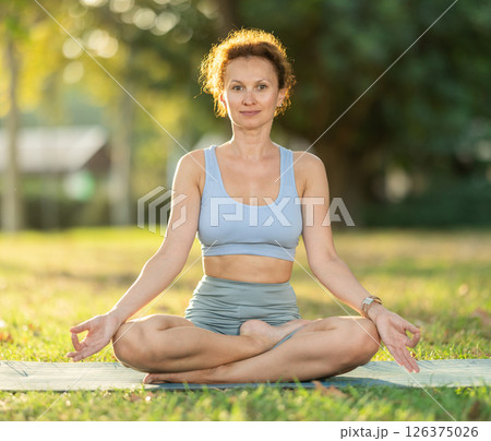 Lotus pose - slim woman doing yoga outdoors in park 126375026