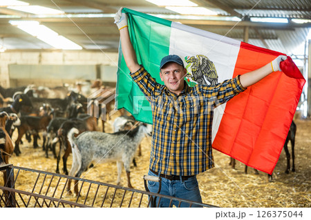 Successful farmer holding Mexican flag in goat pen 126375044