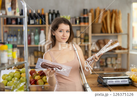 Young woman chooses dried sausage in store Young woman chooses dried sausage in store 126375126