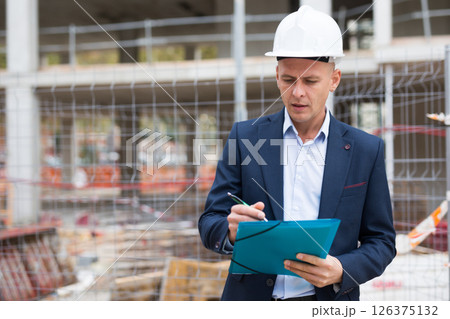 Engineer in suit standing in construction area with folder in hands 126375132
