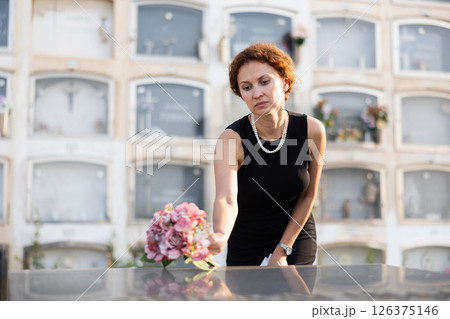 Sorrowful woman puts bouquet of hydrangeas on grave of deceased friend, mourns loss Sorrowful woman puts bouquet of hydrangeas on grave of deceased friend, mourns loss 126375146