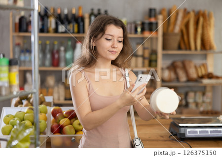 Positive girl purchaser scanning QR code or barcode of cheese in supermarket Positive girl purchaser scanning QR code or barcode of cheese in supermarket 126375150