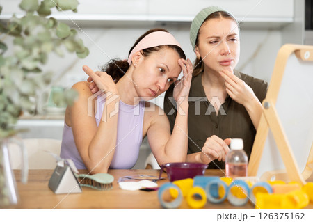 Two female friends examining faces in vanity mirror at home Two female friends examining faces in vanity mirror at home 126375162
