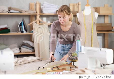 Female dressmaker using fabric shears to cut linen in workshop 126375168