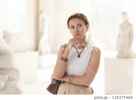 Portrait of woman visitor with smartphone in hands looking exhibition of statues in museum 126375484